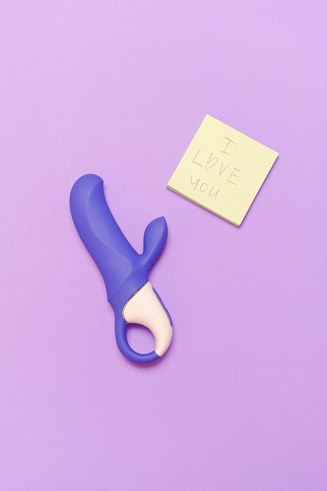 A purple silicone vibrator next to a sticky note saying 'I love you' on a lavender surface.